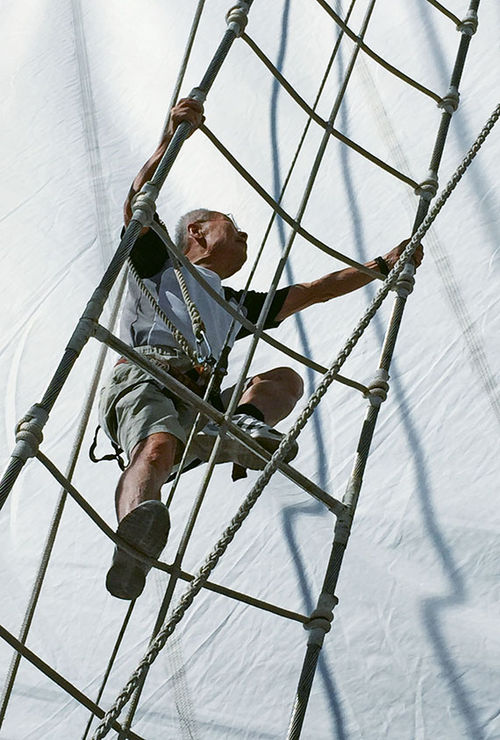 A guest climbs rigging to reach a platform on the ship’s foremast.