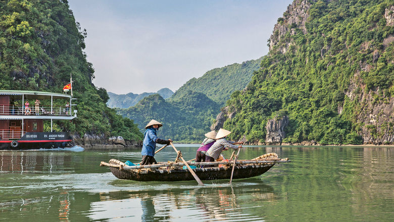 The Angkor Pandaw cruises past a rustic boat and impressive karst formations in Ha Long Bay, Vietnam.