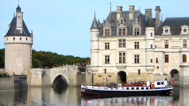 European Waterways' Nymphea hotel barge crusing by Chateau de Chenonceau which spans the River Cher in France.