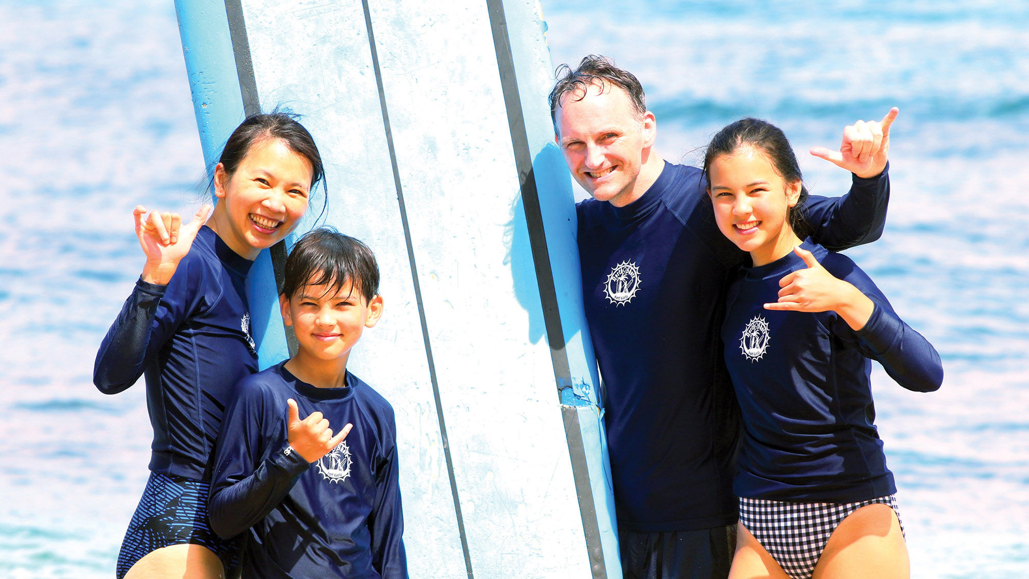 A family taking a North Shore Surf Girls lesson throws up “hang loose” signs.