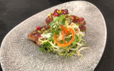 An appetizer of seared diver scallop and cured pork belly confit with orange pomegranate sauce.