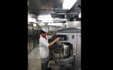A galley worker adjusts the mixer kneading dough for carrot cake on the Empress of the Seas.