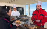 An assistant chef on the Ponant ship Le Lyrail on the deck serving food from a portable grill for the Southernmost BBQ.