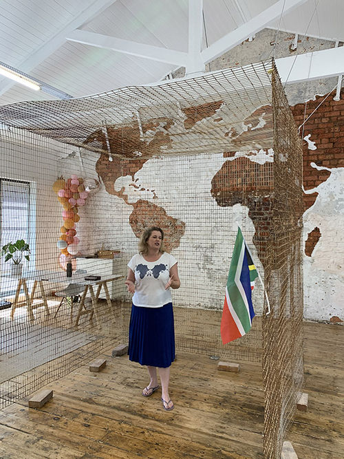 South African artist Chris Swift talks about the art and jewelry she makes with fencing that was torn down from Robben Island. Behind her is an installation using pieces of the fence. South African artist Chris Swift talks about the art and jewelry she makes with fencing that was torn down from Robben Island. Behind her is an installation using pieces of the fence.