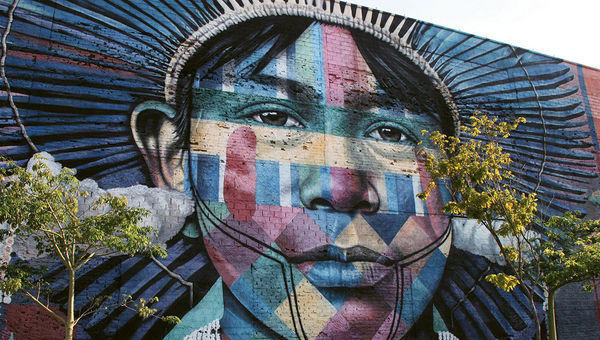 One of five figures representing indigenous peoples from around the globe on the 560-foot-long mural, “Ethnicities,” on the side of a warehouse in Rio’s rejuvenated port district. The face represents an Amazonian tribe. One of five figures representing indigenous peoples from around the globe on the 560-foot-long mural, “Ethnicities,” on the side of a warehouse in Rio’s rejuvenated port district. The face represents an Amazonian tribe.