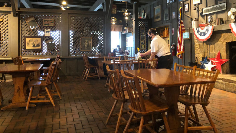 A masked waitress sanitizes a table at a Cracker Barrel Country Store restaurant in Crestview, Fla. Allowing inside dining is part of the reopening of Florida's economy promoted by Gov Ron DeSantis.
