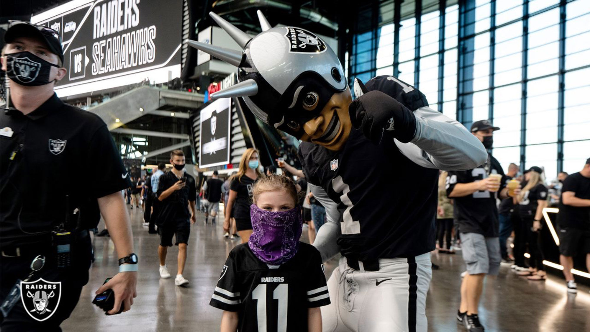 Raider Rusher greets a young Raiders' fan during a preseason game on Aug. 14, the first-time fans were allowed to see the NFL team in person at Allegiant Stadium. The Raiders will require proof of vaccination to attend regular-season games; kids not eligible for the jab will need to wear masks..