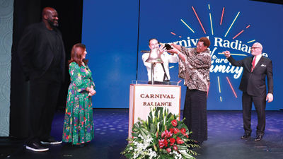 Author and philanthropist Lucille O’Neal pours Champagne on a ship's bell as part of the naming ceremony for Carnival Cruise Line’s Carnival Radiance. In attendance were, at left, O'Neal's son, Carnival Chief Fun Officer Shaquille O’Neal, and Carnival president Christine Duffy, and Carnival Corp. CEO Arnold Donald, right.