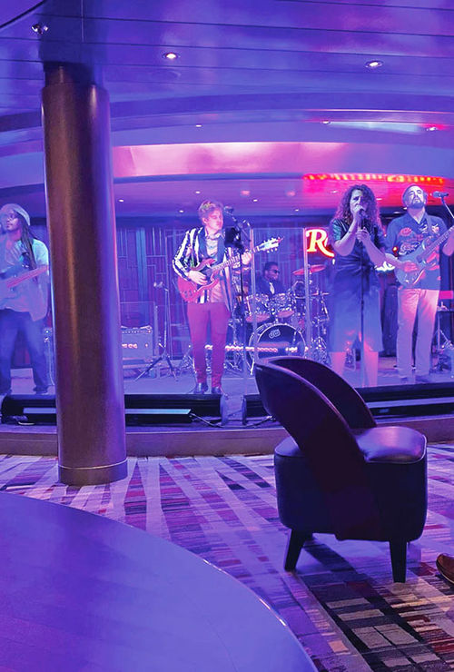 A cover band at the Rolling Stone Rock Room is lit up by colorful lights during a performance.