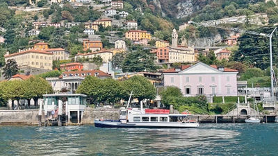 A public ferry sails Lake Como with a hillside view of the luxury lakeside city in the background.