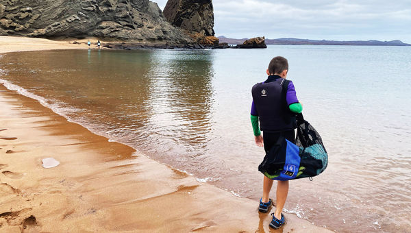 A child lugs snorkeling gear on the beach on Bartolome Island in the Galapagos.
