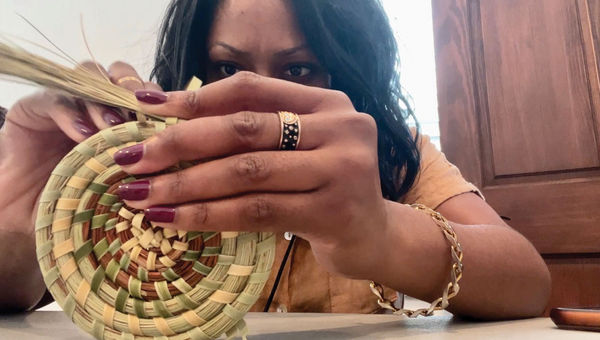 Nicole Edenedo tries her hand at weaving the beginnings of a sweetgrass basket.