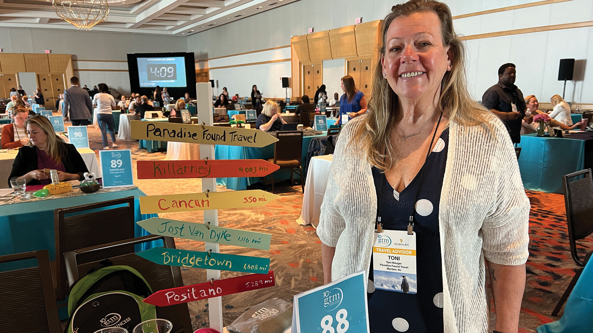 Toni Mauger of Paradise Found Travel in Marlton, N.J., at her table. Her signpost represents some of her favorite destinations, but she has a special place in her heart for Jost Van Dyke in the British Virgin Islands.