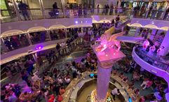 The cruise director speaks to guests in the Carnival Venezia's atrium to recognize the ship's officers.