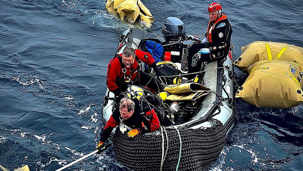 Crew on a dinghy reach for equipment that might help raise the nose of the platform. OceanGate CEO Stockton Rush, in a black scuba suit, sits at the rear.