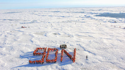 Guests on Ponant's Le Commandant Charcot, in orange, and ship staff, in blue, pose for a photo on an ice floe after reaching 90 degrees north, the geographic North Pole.