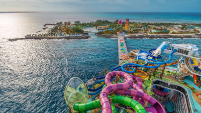 A tangle of colorful waterslides on the Icon of the Seas with Perfect Day at CocoCay in the background.