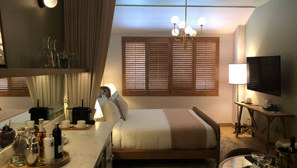 A room at Palihouse Hyde Park Village features green and beige decor and plantation shutters.