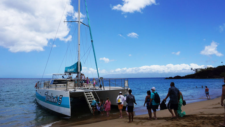 Guests line up and take turns boarding the catamaran, being careful to time it with the waves.