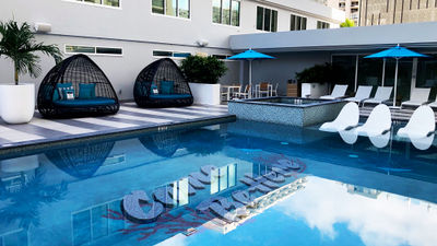 The Outrigger Waikiki Paradise Hotel pool area has been updated with new daybeds and lounge chairs. At the bottom of the pool is a mural that says, "Come Be Here."