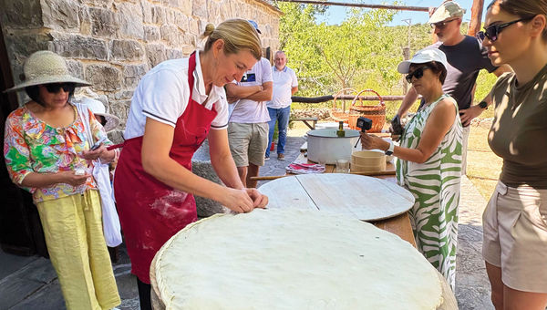 Travelers watch as a woman seals the dough before baking soparnik, a traditional savory pie from the Dalmatian region. Travelers watch as a woman seals the dough before baking soparnik, a traditional savory pie from the Dalmatian region.