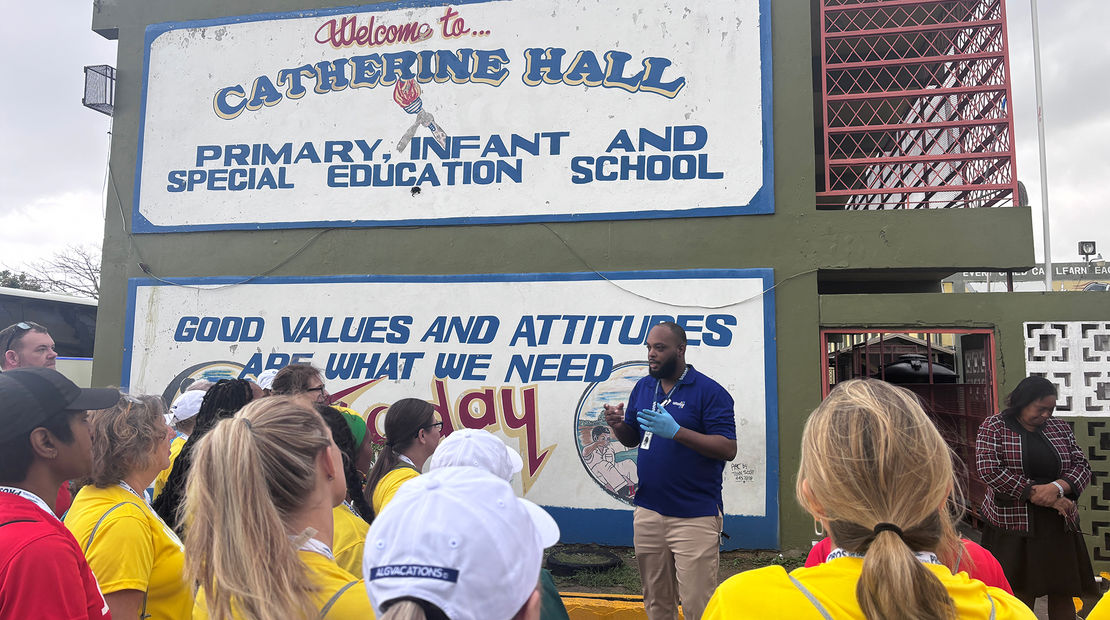 Volunteering travel advisors listen to instructions outside of Catherine Hall Primary School, where they paint and organize donations.