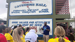 Volunteering travel advisors listen to instructions outside of Catherine Hall Primary School, where they paint and organize donations.