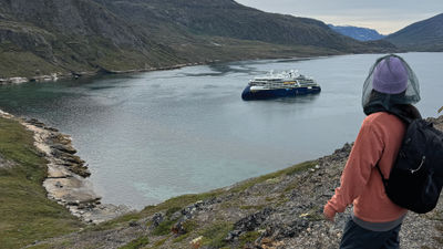 A passenger on a National Geographic-Lindblad Expeditions Greenland cruise looks down at the National Geographic Resolution during a hike.