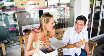 A couple enjoys malasadas, a Portuguese pastry similar to a doughnut, at Leonard's Bakery, which is on the Taste of Oahu food tour offered by Aunty Sweetie's Hawaiian Tours.