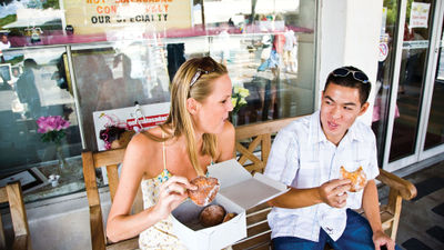 A couple enjoys malasadas, a Portuguese pastry similar to a doughnut, at Leonard's Bakery, which is on the Taste of Oahu food tour offered by Aunty Sweetie's Hawaiian Tours.