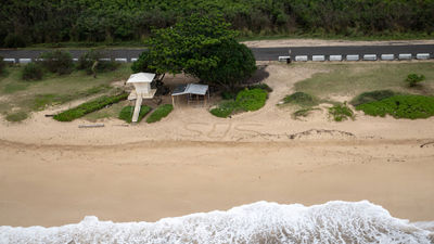 The Coast Guard flies over an SOS written in the sand at Yokohama Bay, Oahu, March 21. With flooding easing, visitors are asked to be mindful of recovery efforts around the state.