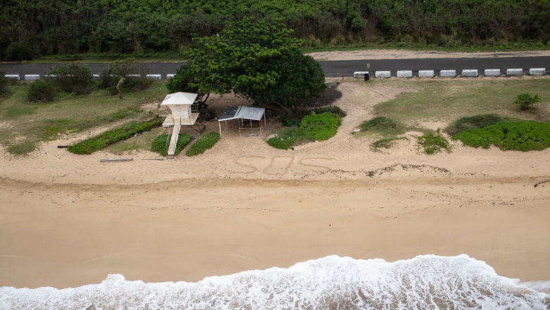 The Coast Guard flies over an SOS written in the sand at Yokohama Bay, Oahu, March 21. With flooding easing, visitors are asked to be mindful of recovery efforts around the state.