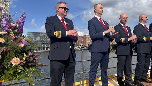Trafalgar Verity crew members stand on the ship's sun deck with vases of water from an Amsterdam canal.