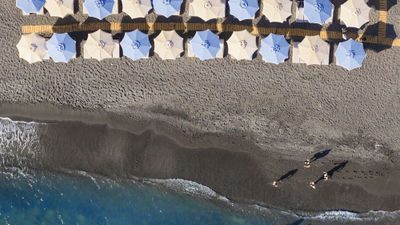 The Royal Beach Club Santorini features black sand, loungers with umbrellas and a DJ.