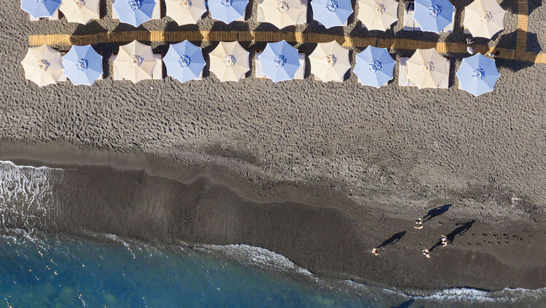 The Royal Beach Club Santorini features black sand, loungers with umbrellas and a DJ.