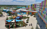 Guests enter the park at the Isle of Curiosity, home to the Universal Kids Resort Cafe and the Universal Kids Resort Store as well as Gabby's Cat-Tastic Dance Party! and Cakey's Cupcakes, featuring characters from "Gabby's Dollhouse." The hotel is the building on the right, illustrating its proximity to the park.