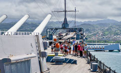 Visitors onboard the Battleship Missouri Memorial in 2024, with the USS Arizona Memorial in the background.