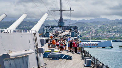 Visitors onboard the Battleship Missouri Memorial in 2024, with the USS Arizona Memorial in the background.