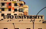 Signage for a Tirana university (UFO stands for Universitas Fabrefacta Optime), with apartment buildings in the background.