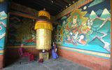A woman turns a wheel covered in gold leaf at the entrance of Trongsa Dzong.