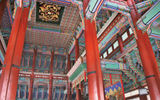Interior of the king's audience hall at Seoul's Gyeongbok Palace, with brightly painted wood ceiling elements and very red pillars.