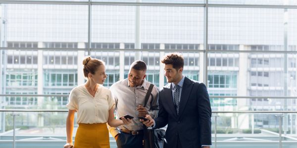Three professionals chat in a bright glass-walled lobby.