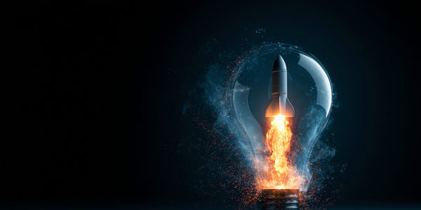 Abstract rocket launching inside a glowing light bulb surrounded by particle effects, innovation and idea concept, creative technology visual, with copy space