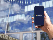 Expedia mobile travel booking application displayed on smartphone held in male hand near modern office building