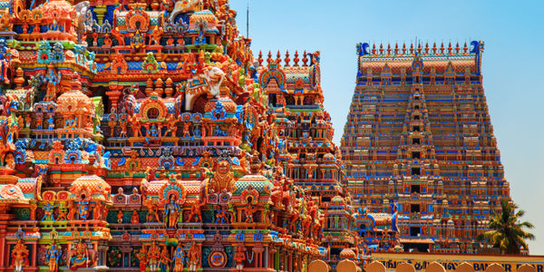 A vibrant Hindu temple complex with ornate, multicolored gopurams against a clear blue sky.