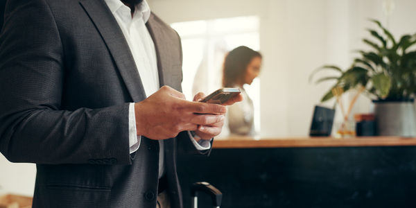 Hotel, luggage or hands of businessman with phone for online checkin, check booking or reservation. Professional, guest and smartphone in lobby for conference schedule, chat and email travel agency.