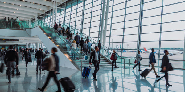 A busy airport terminal with travelers walking and using a glass staircase.