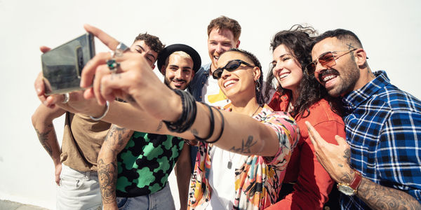 Group of happy young friends having fun and laughing while taking a selfie with mobile phone. Diverse millennial people spending time together. Friendship concept. Real people lifestyle.
