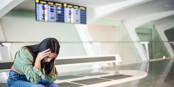 sad and dejected girl on the airport bench with her luggage because her flight has been canceled