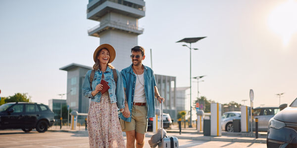 Happy couple with passports and suitcase going to airport terminal. Copy space.